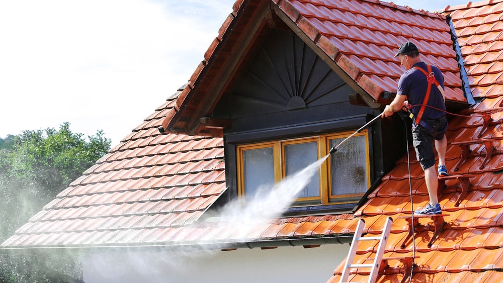 Bilde av en renholder som holder en høytrykksspyler og vasker taket, strålen på spyleren har middels styrke - Midt-Norsk Vask AS - Fasadevask