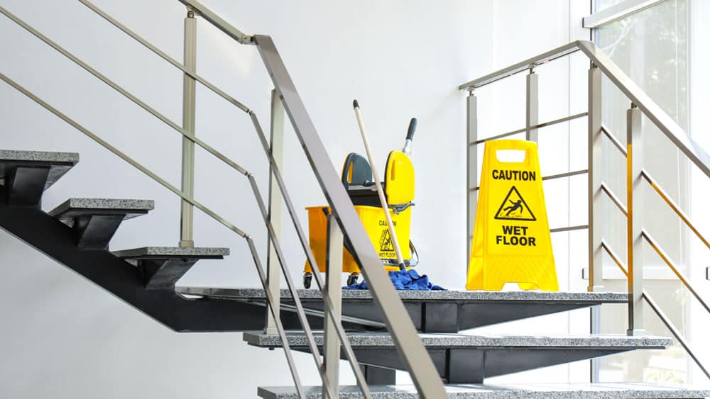 Bilde av vaskeutstyr i en trapp, det står et skilt hvor det står "Caution - Wet floor" - Midt-Norsk Vask AS - Fasadevask